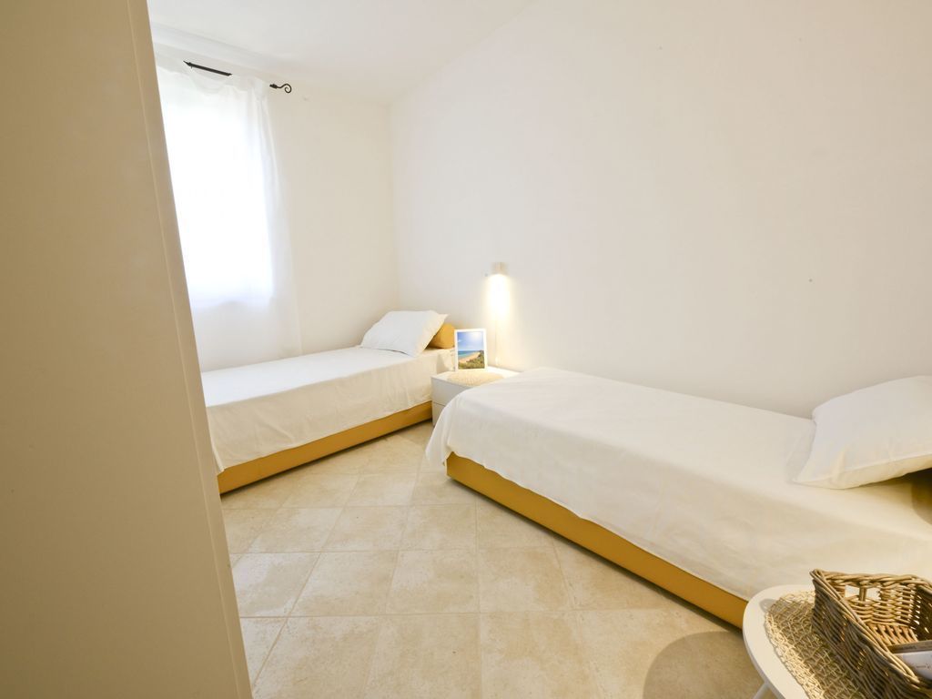 A bedroom with two single beds, a bedside table with a lamp, and a small wicker basket on the floor.