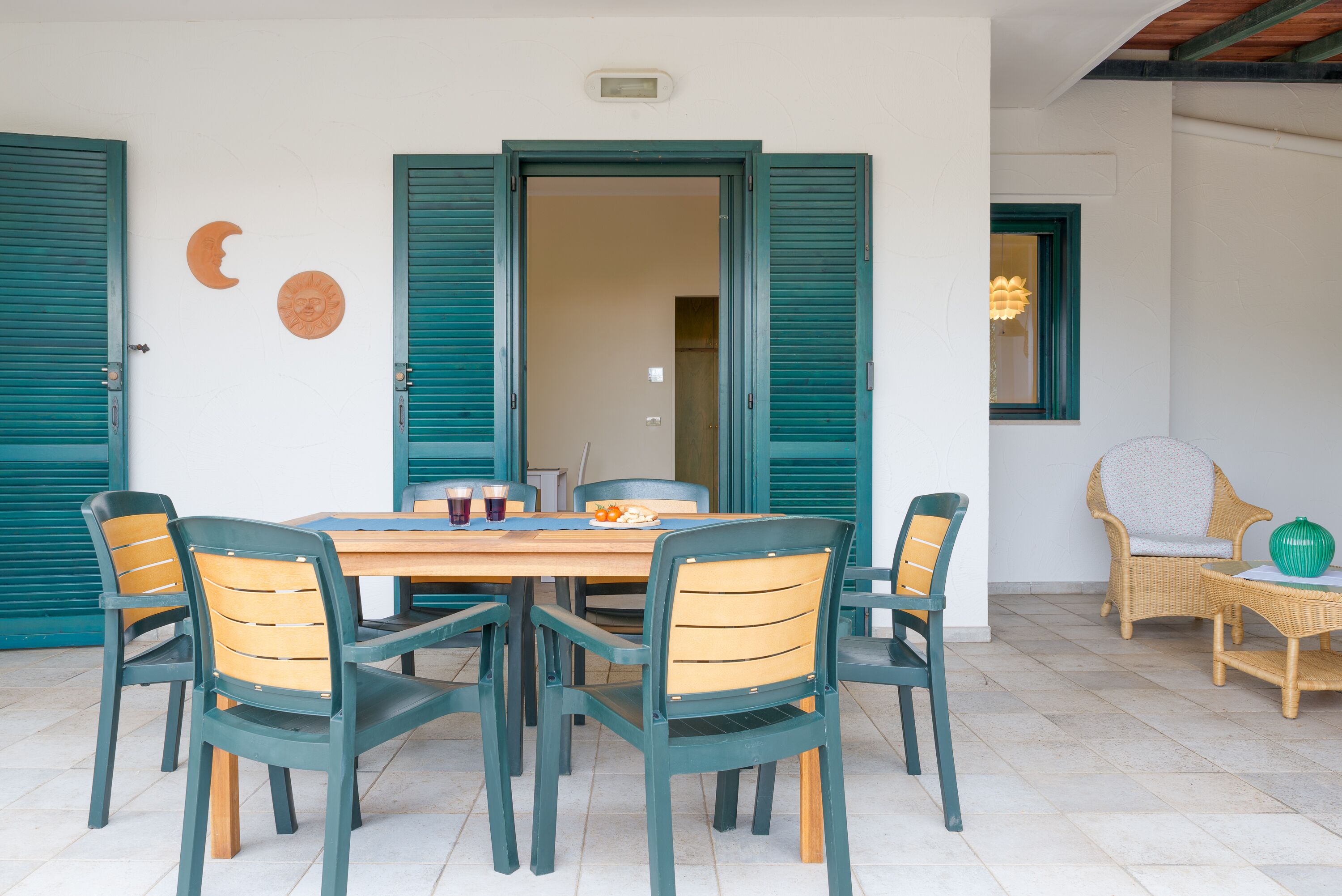A dining area with a wooden table and chairs, a window with a view, and a door with green shutters.