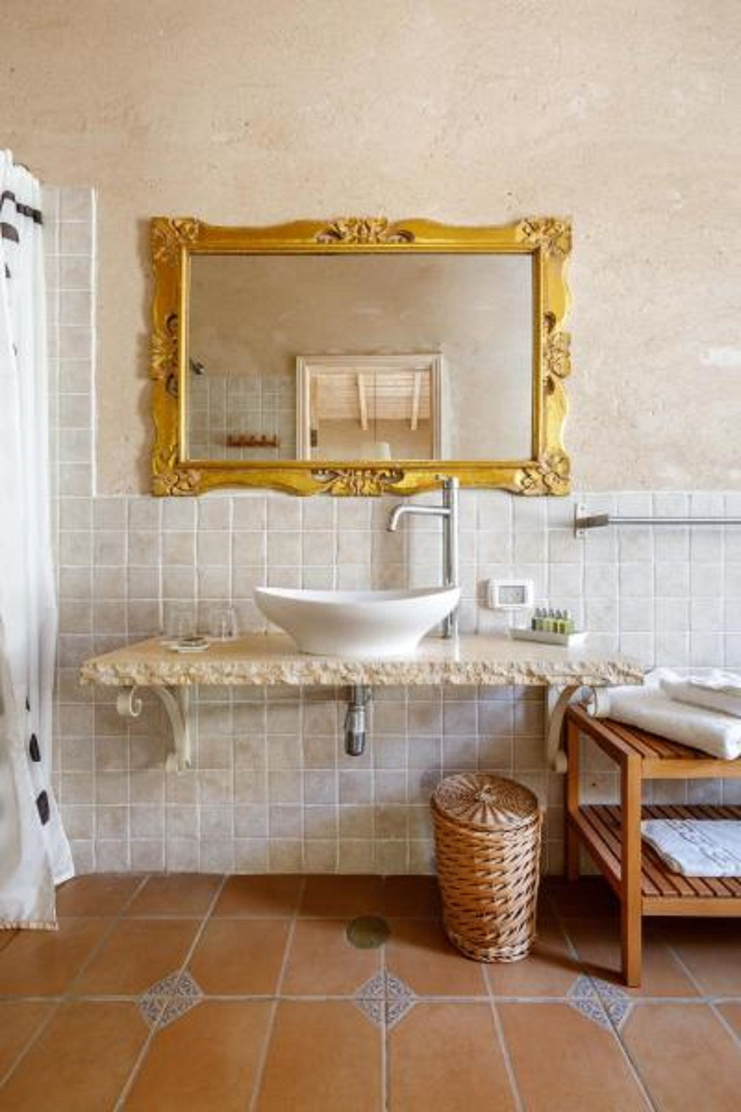 Un baño con un lavamanos blanco, un espejo con marco dorado y piso de baldosas.