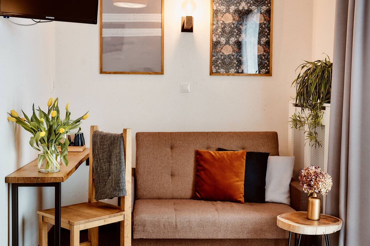 Una sala acogedora con un sofá, una mesita con un florero y un televisor montado en la pared.
