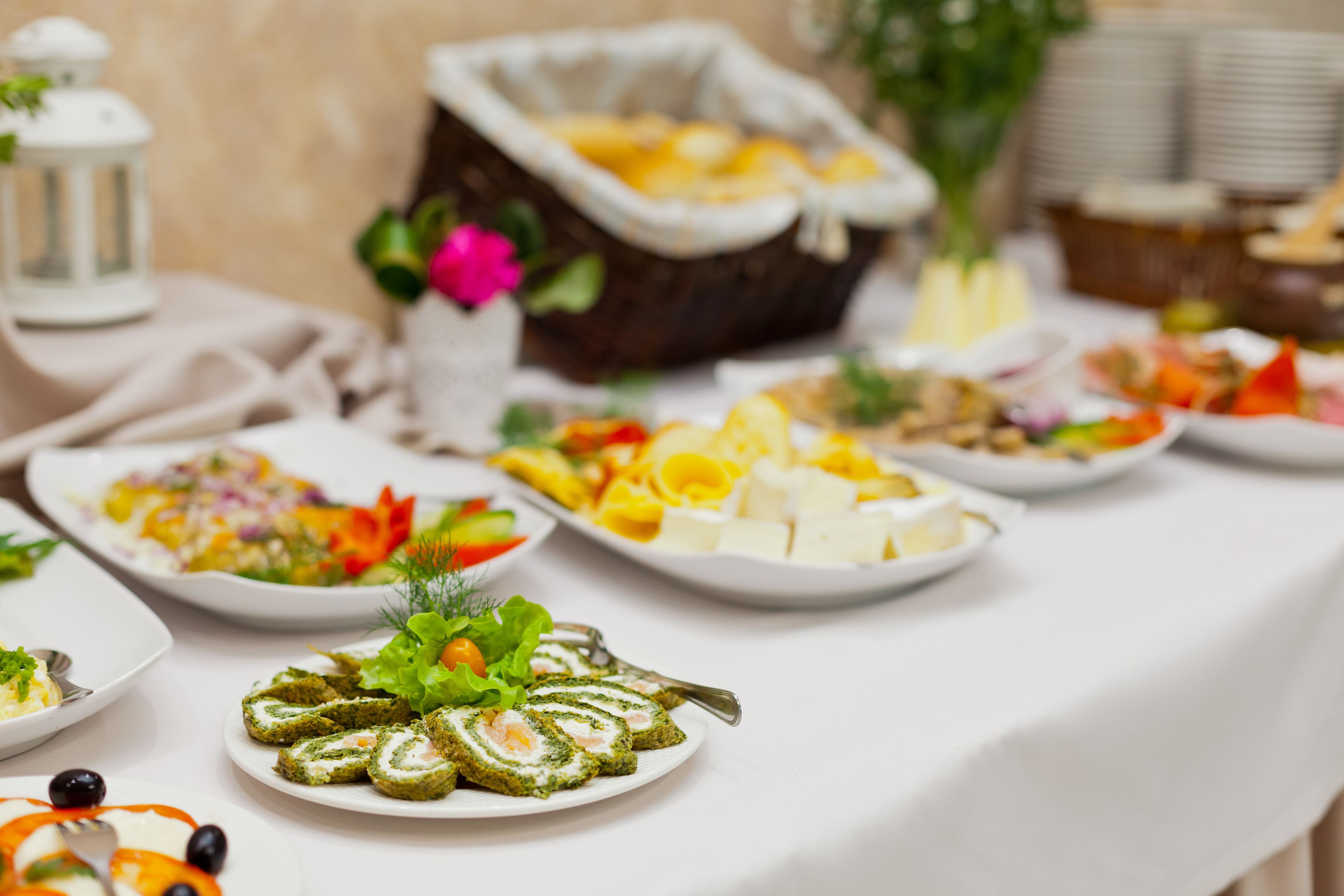 A buffet table with various dishes, including a plate of rolled meat, salads, and cheese.