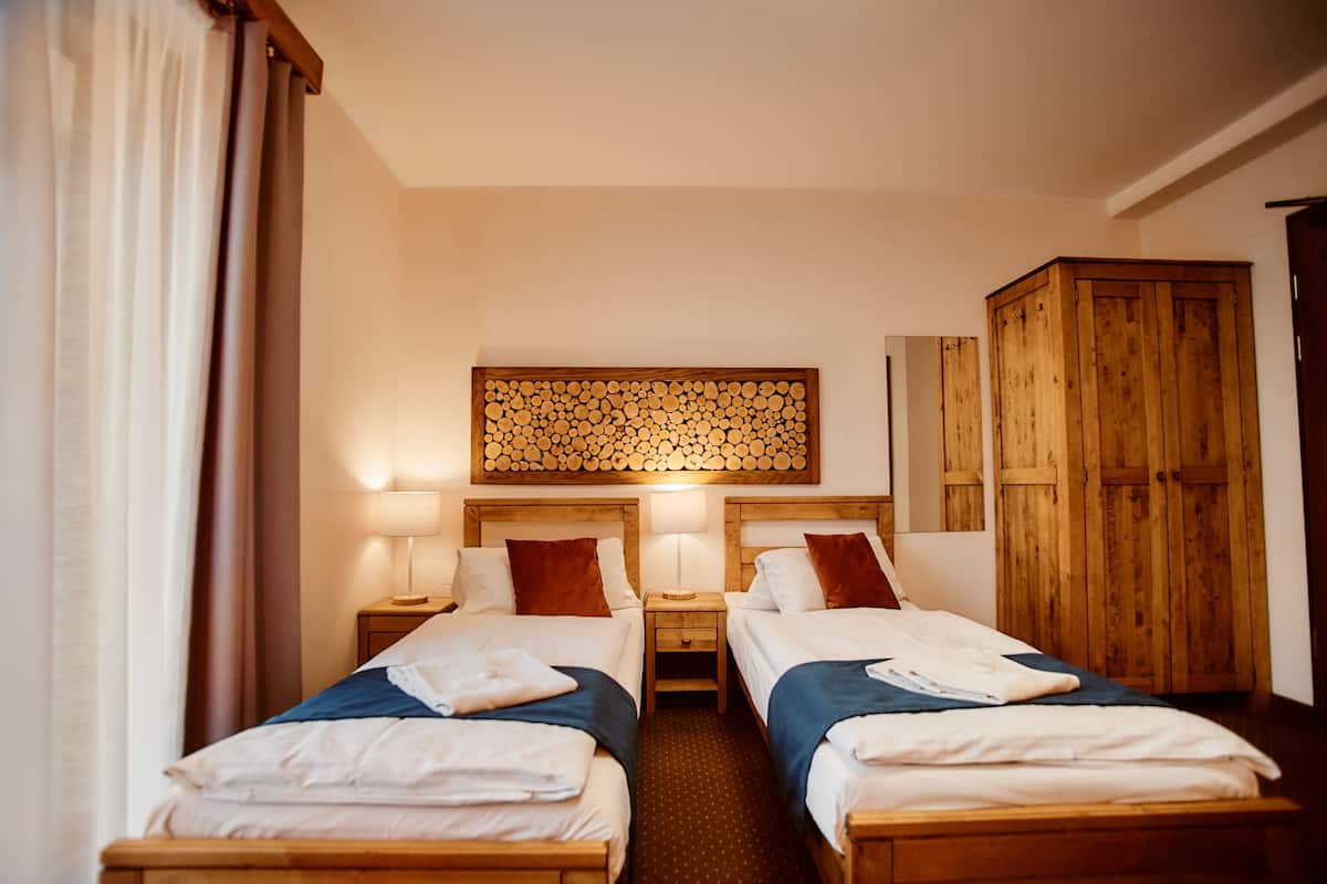 Habitación de hotel con dos camas individuales, cabeceros de madera, un armario de madera y un panel de madera montado en la pared.