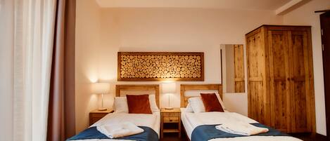A hotel room with two single beds, wooden headboards, a wooden wardrobe, and a wall-mounted wooden panel.