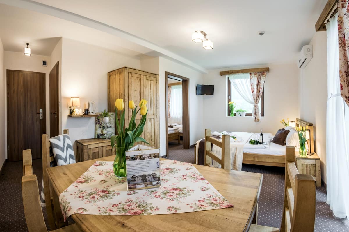 Una habitación acogedora con una mesa de comedor de madera, una cama con cabecero de madera, una pequeña cocina americana y un televisor montado en la pared.