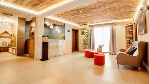 A reception area with a wooden ceiling, a reception desk, a seating area with a sofa and ottoman, and a bookshelf. - Perła Beskidu (Ustron)