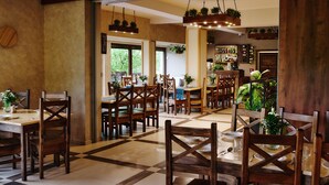 A spacious dining area with wooden tables and chairs, a bar area with a variety of bottles, and hanging plants. - Perła Beskidu (Ustron)
