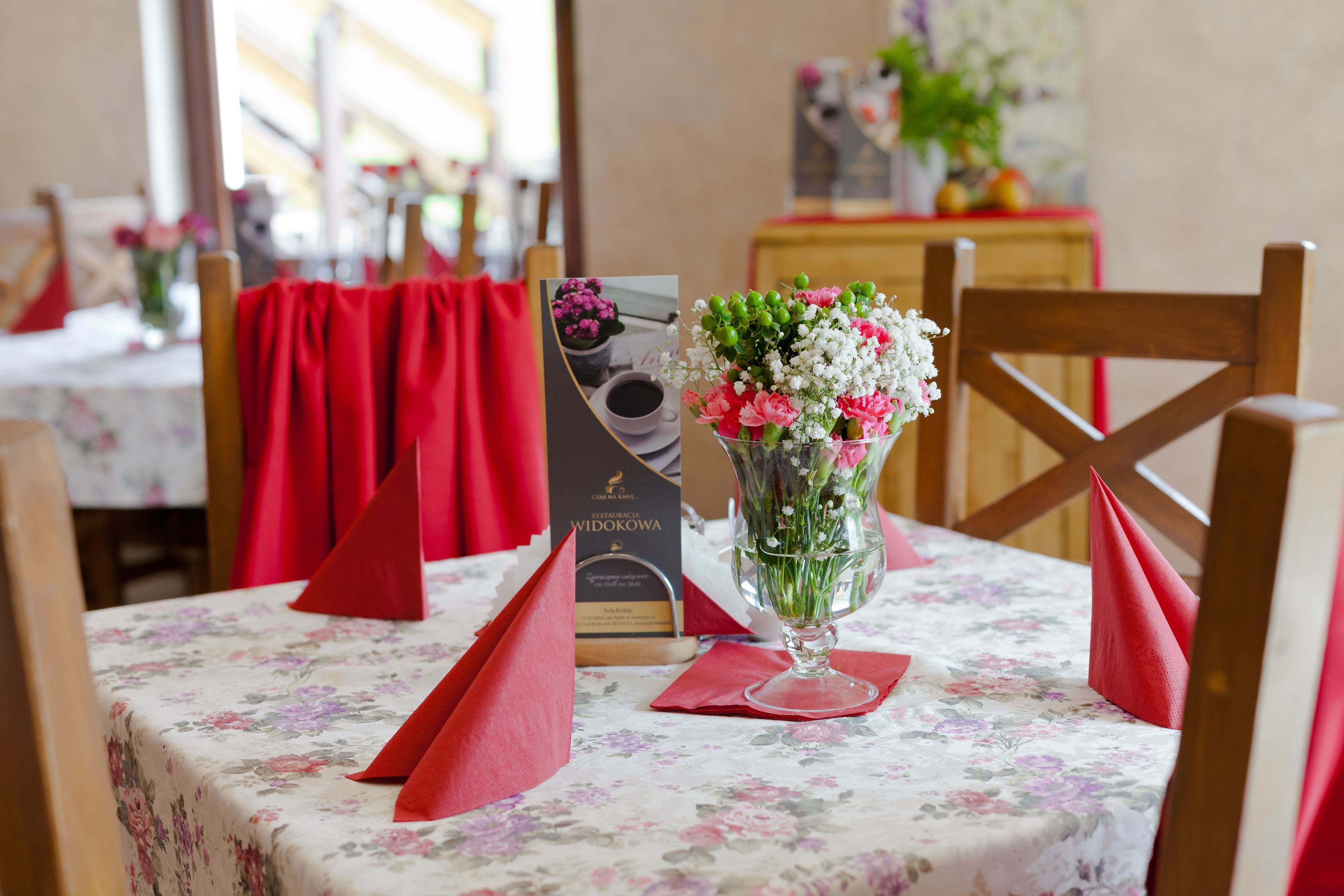 Uma mesa de jantar com toalha de mesa florida, guardanapos vermelhos e um vaso de flores.