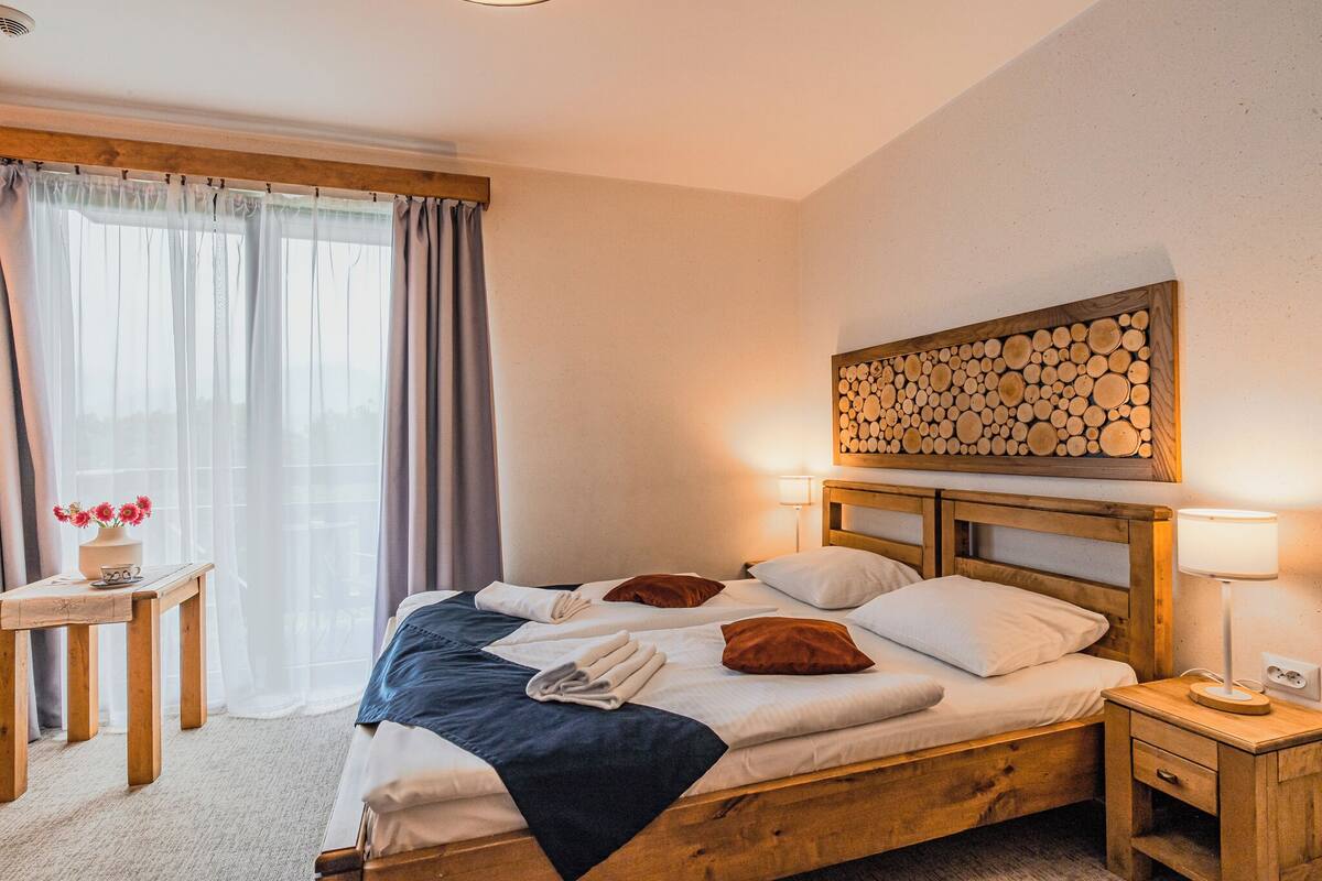 Una cama bien hecha con cabecera de madera, una mesita de noche con lámpara y un adorno de leña montado en la pared.