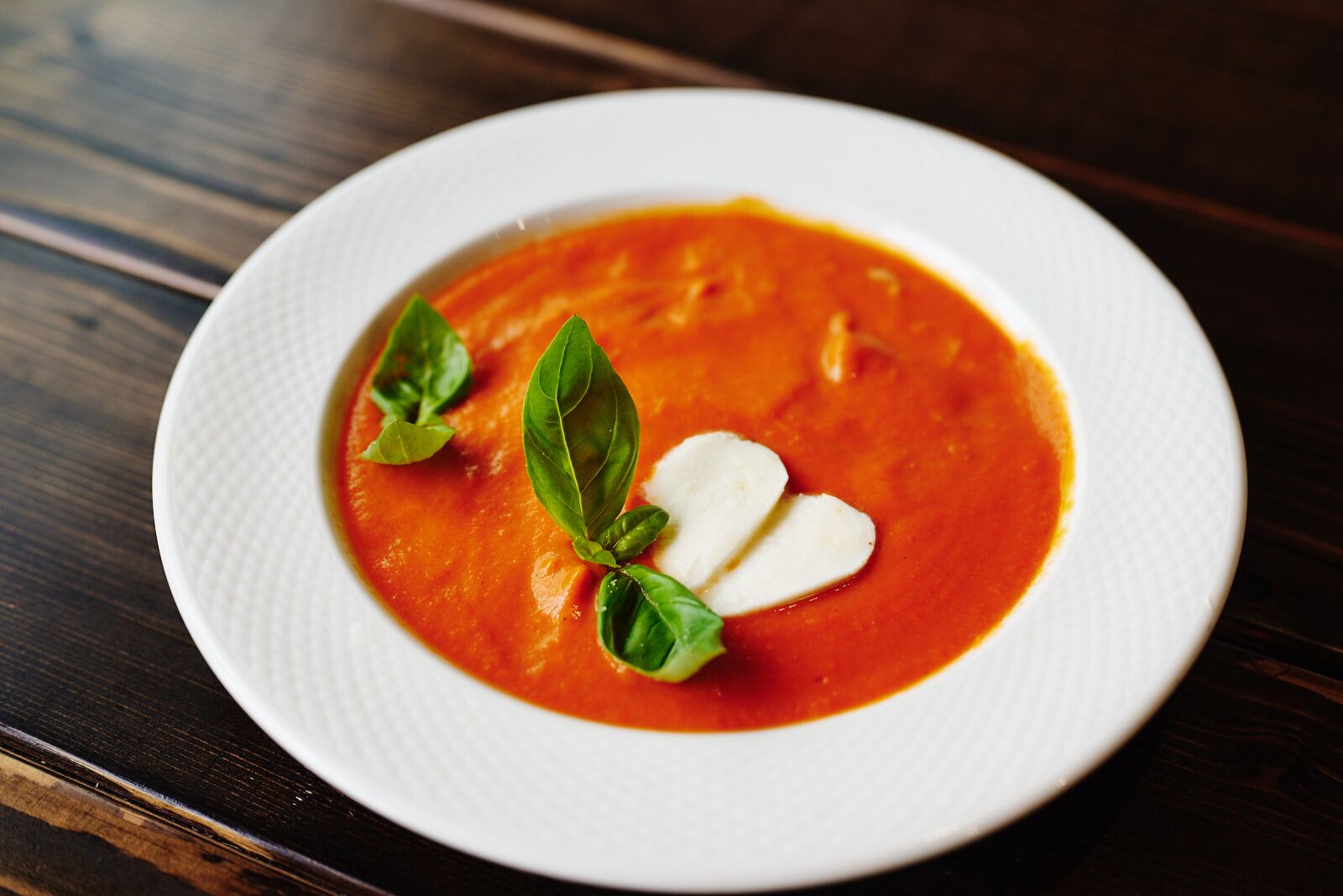 Un plat blanc amb sopa vermella, decorada amb fulles de bàsil i una culleradeta de crema.