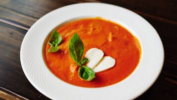 Un plat blanc amb sopa vermella, decorada amb fulles de bàsil i una culleradeta de crema.