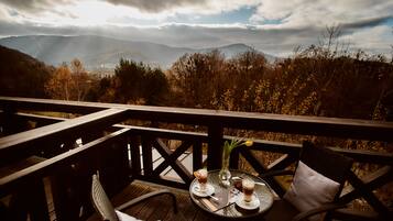 A wooden deck with a table and chairs, overlooking a mountainous landscape.