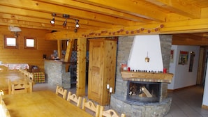 A wooden interior with a dining area, a stone fireplace, and a kitchen visible through an open door. - Central Hostel Châtel (Chatel)
