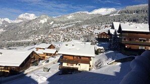 A snow-covered village with wooden buildings, a ski slope, and mountains in the background. - Central Hostel Châtel (Chatel)