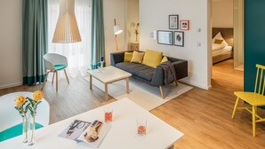 A modern living room with a sofa, coffee table, and chairs. There is a dining table with a magazine and glasses. A bed is visible in the background. - Goldkind Feine Wohn & Schlafstuben (Heppenheim)