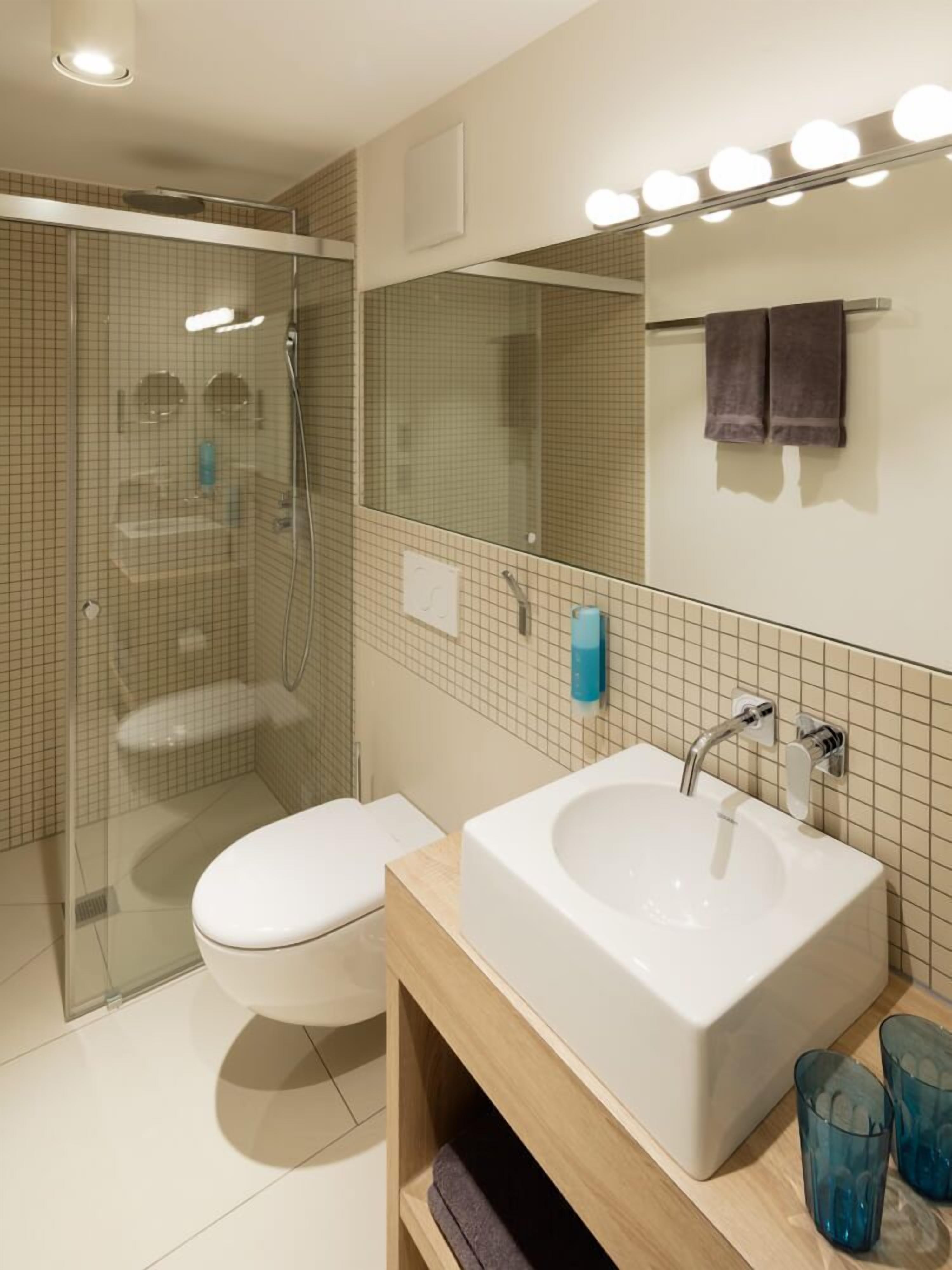 A modern bathroom with a glass-enclosed shower, a white toilet, a large sink with a mirror above, and a towel rack with two towels.