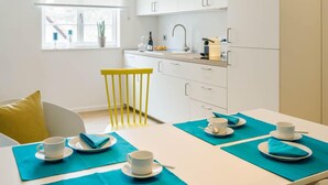 A modern kitchen with white cabinets, a yellow chair, and a dining table set with blue placemats and white plates. - Goldkind Feine Wohn & Schlafstuben (Heppenheim)