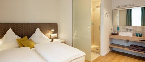 A hotel room with a large bed, a nightstand, a bathroom with a sink and mirror, and a wooden floor.