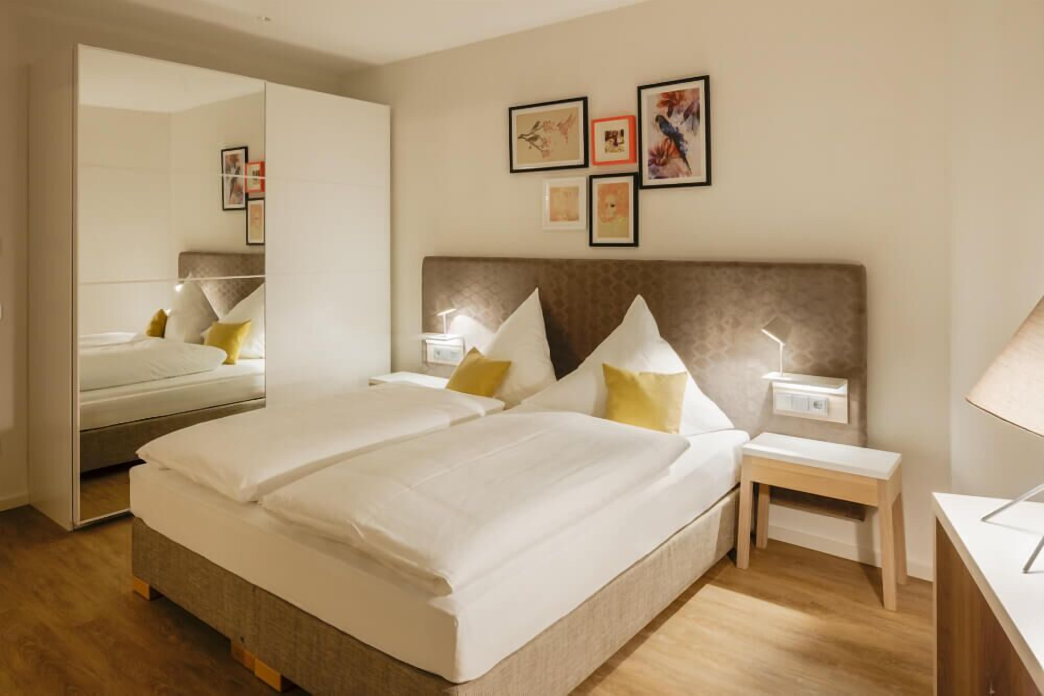 A hotel room with a large bed, bedside tables, a mirror, and artwork on the wall.