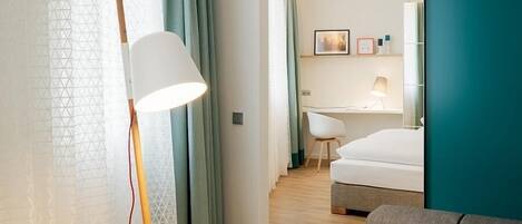Una habitación de hotel moderna con un sofá gris, una lámpara de pie, una cama y un escritorio con una silla.