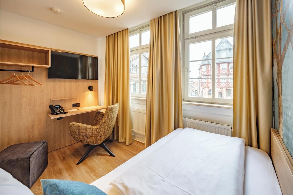 A hotel room with a bed, a desk with a telephone, a chair, and a TV mounted on the wall.