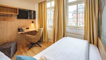 A hotel room with a bed, a desk with a telephone, a chair, and a TV mounted on the wall.