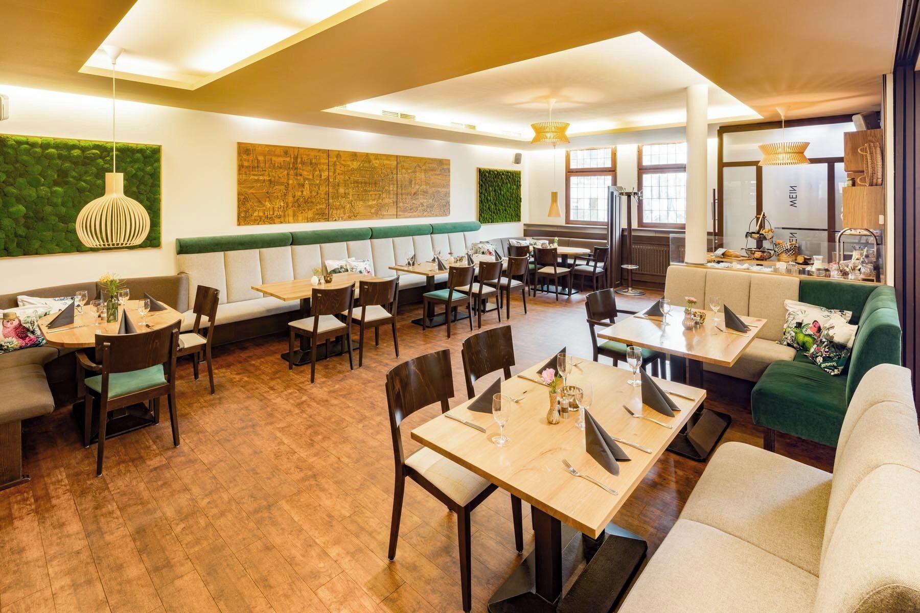 Un restaurante con mesas de madera, asientos acolchados y una pared verde decorada con obras de arte.
