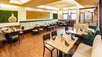 Un restaurante con mesas de madera, asientos acolchados y una pared verde decorada con obras de arte.
