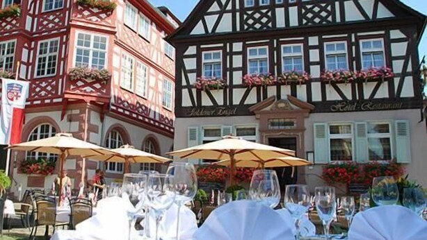 A traditional European building with a half-timbered facade, outdoor dining area with tables and umbrellas, and a sign indicating a restaurant. - Goldener Engel Hotel - Restaurant (Heppenheim)