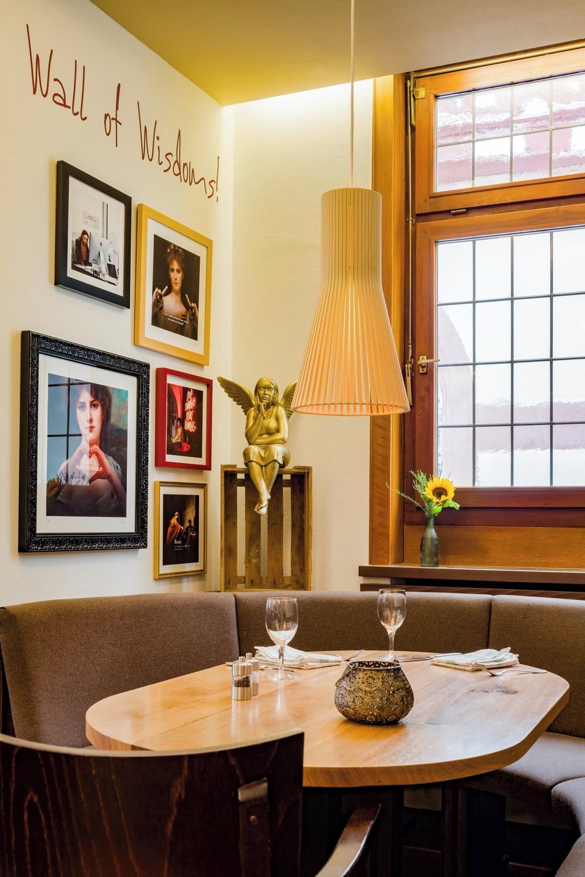 A dining area with a round table, chairs, a wall with framed pictures, a decorative angel sculpture, and a window with a view.