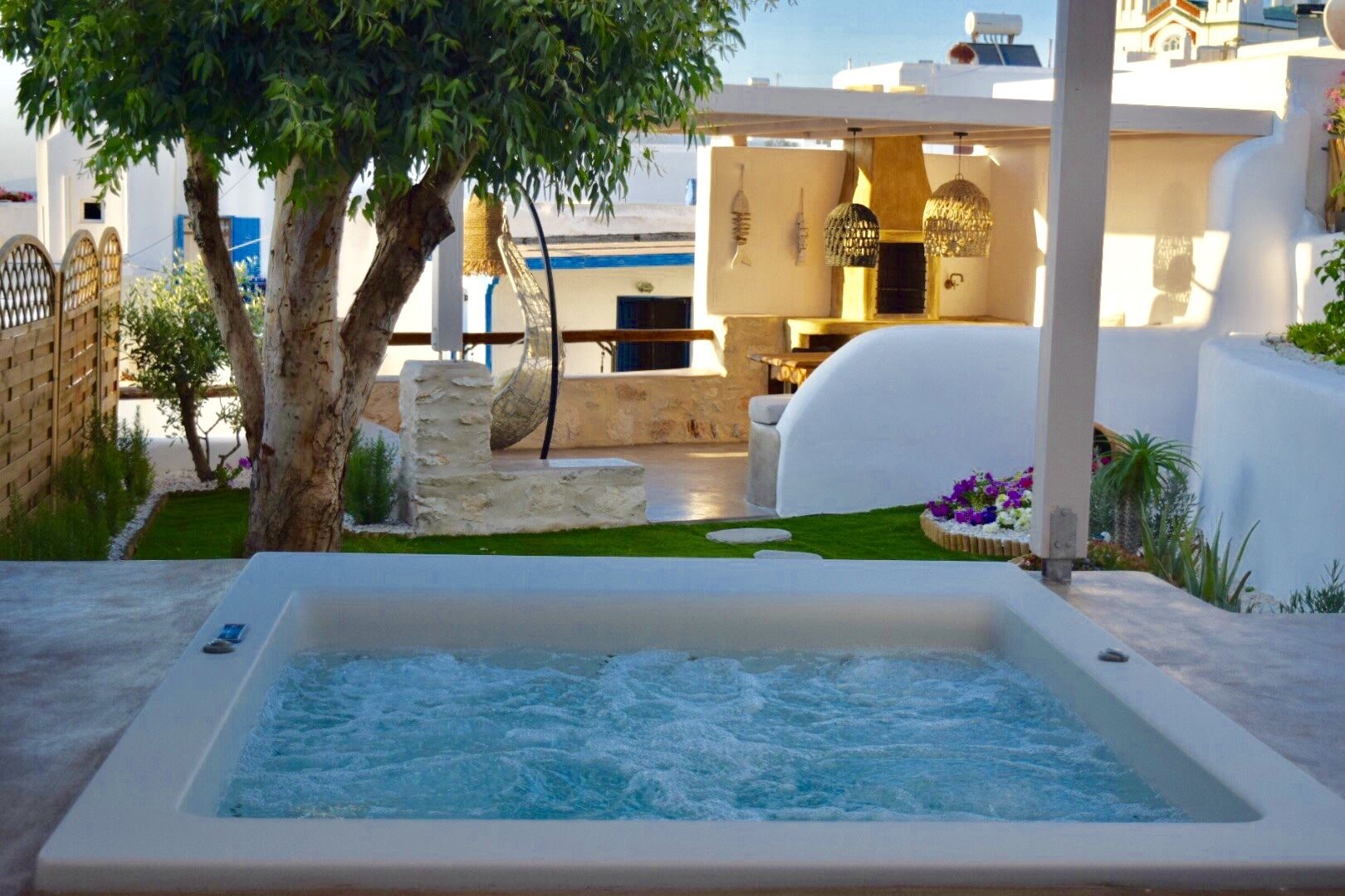 A spa area with a hot tub, a stone bench, and a pergola with hanging lights.