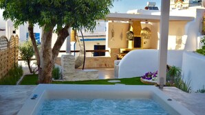 A spa area with a hot tub, a stone bench, and a pergola with hanging lights. - Aegis Royale Villa (Paros)