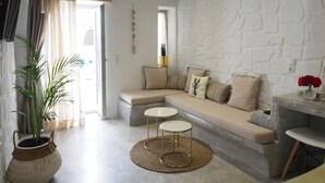 A modern living room with a stone wall, a beige sofa, two small round tables, and a large potted plant. - Aegis Royale Villa (Paros)