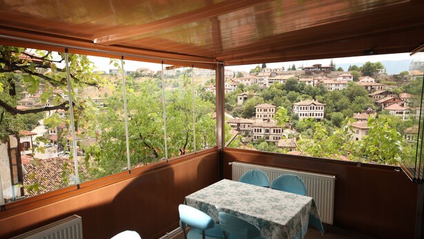 A balcony with a table and chairs, overlooking a residential area with houses and trees. - Efe Guest House (Safranbolu)