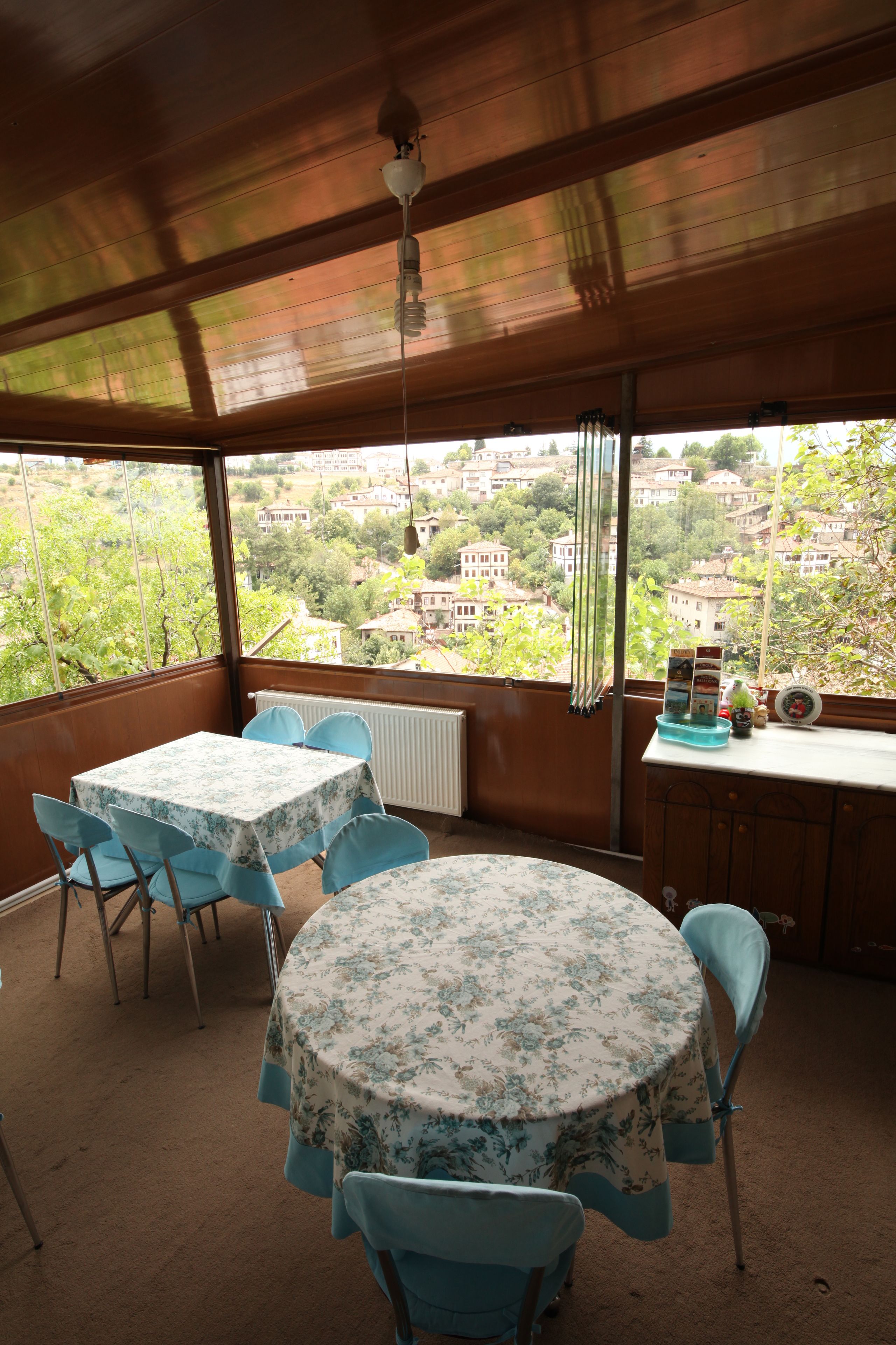 A covered outdoor dining area with a table and chairs, a view of the surrounding buildings, and a radiator.