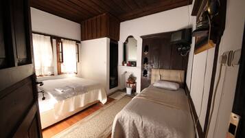 A room with two beds, wooden ceiling, and a small bathroom with a toilet and sink.