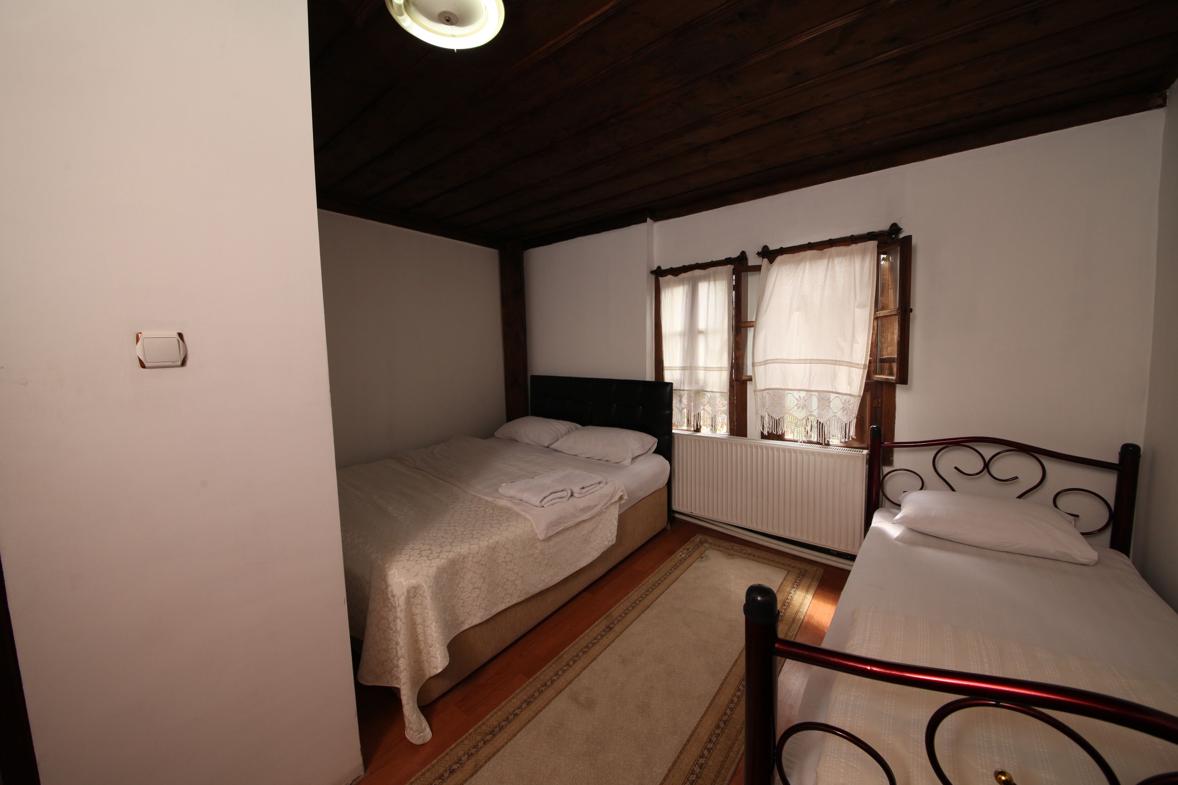 Una habitación con dos camas individuales, techo de madera, radiador y ventana con cortinas.