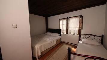 Una habitación con dos camas individuales, techo de madera, radiador y ventana con cortinas.