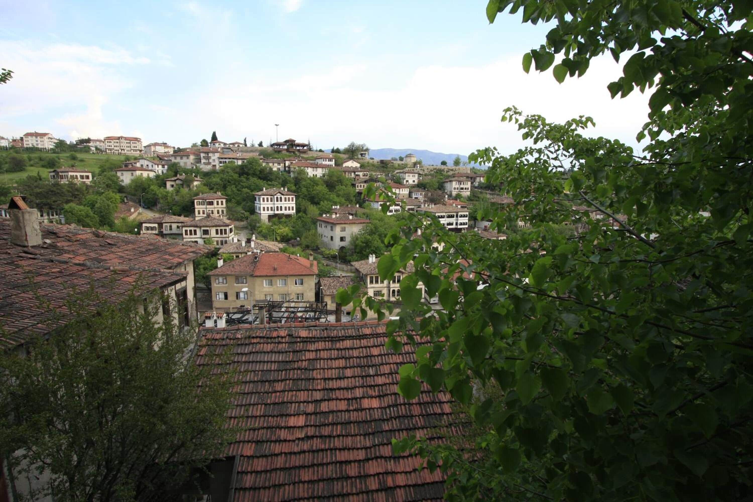 Un pueblo en una colina con edificios de tejados de teja y abundante vegetación, bajo un cielo despejado.