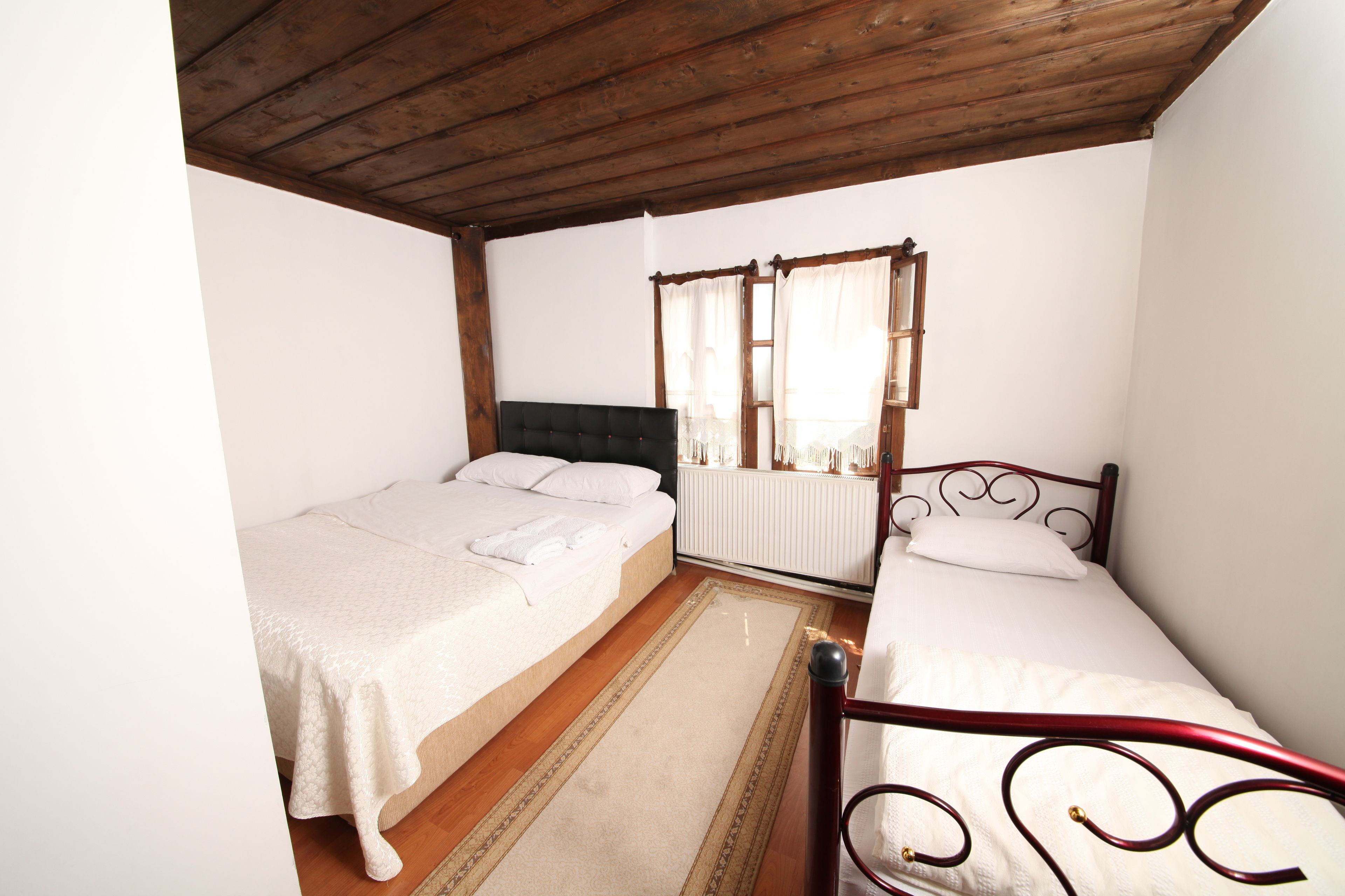 A bedroom with two single beds, a wooden ceiling, a radiator, and a window with curtains.
