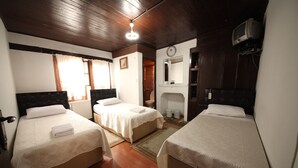 A room with two single beds, wooden flooring, a mirror, a clock, and a television on the wall. - Efe Guest House (Safranbolu)