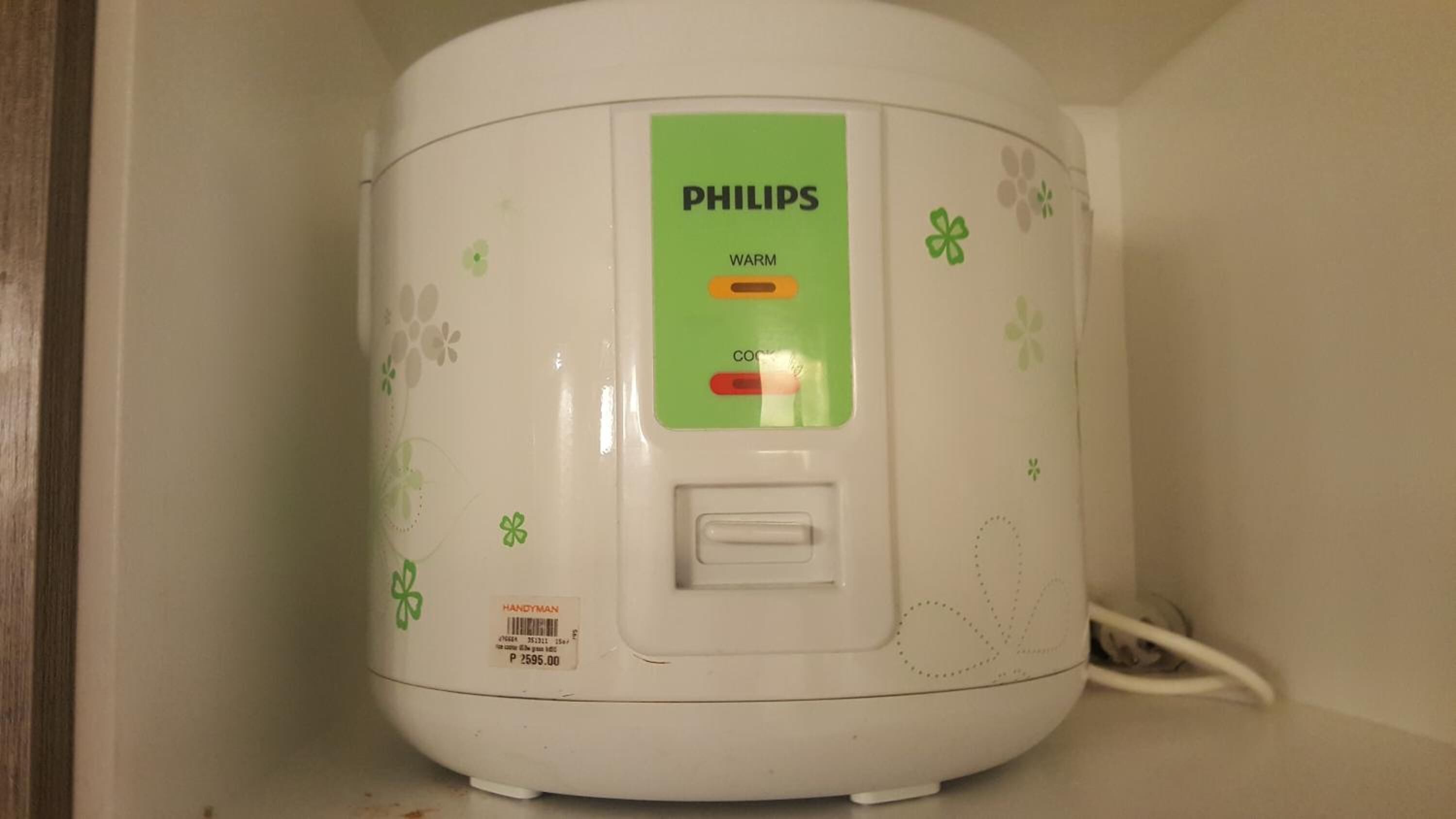 A white Philips rice cooker with a green label, a power cord, and a price tag.