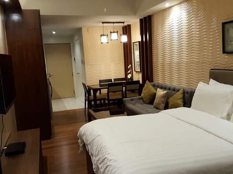 A hotel room with a large bed, a sofa, a dining table with chairs, and a TV.