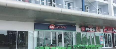 A multi-story building with a DQ Express restaurant on the ground floor, green chairs outside, and a Pizza Hut across the street.