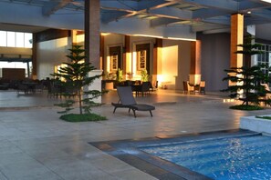A spacious indoor area with a pool, lounge chairs, and seating areas.