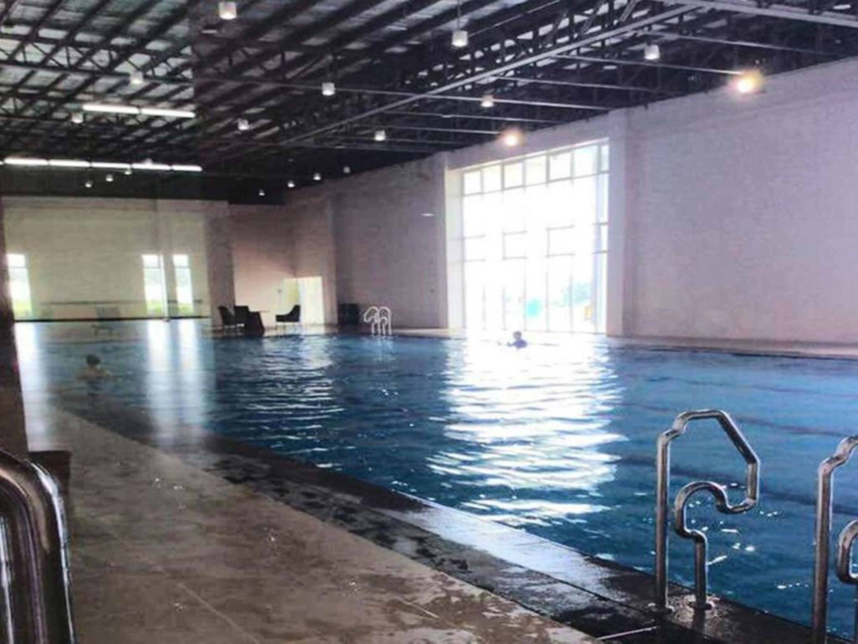 Una piscina interior con agua cristalina, un trampolín y un techo alto con vigas a la vista.