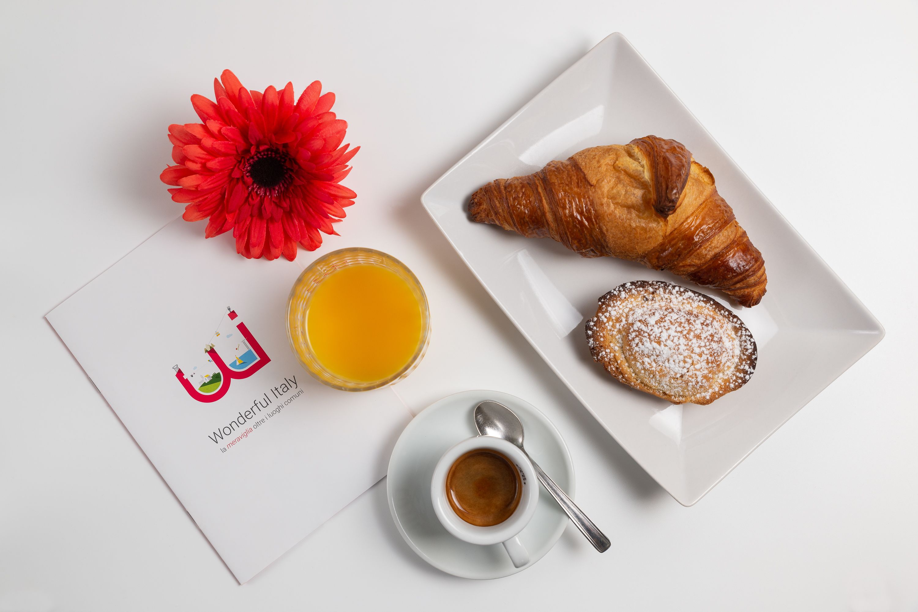 A breakfast setting with a croissant, a pastry, a glass of orange juice, a flower, and a menu.