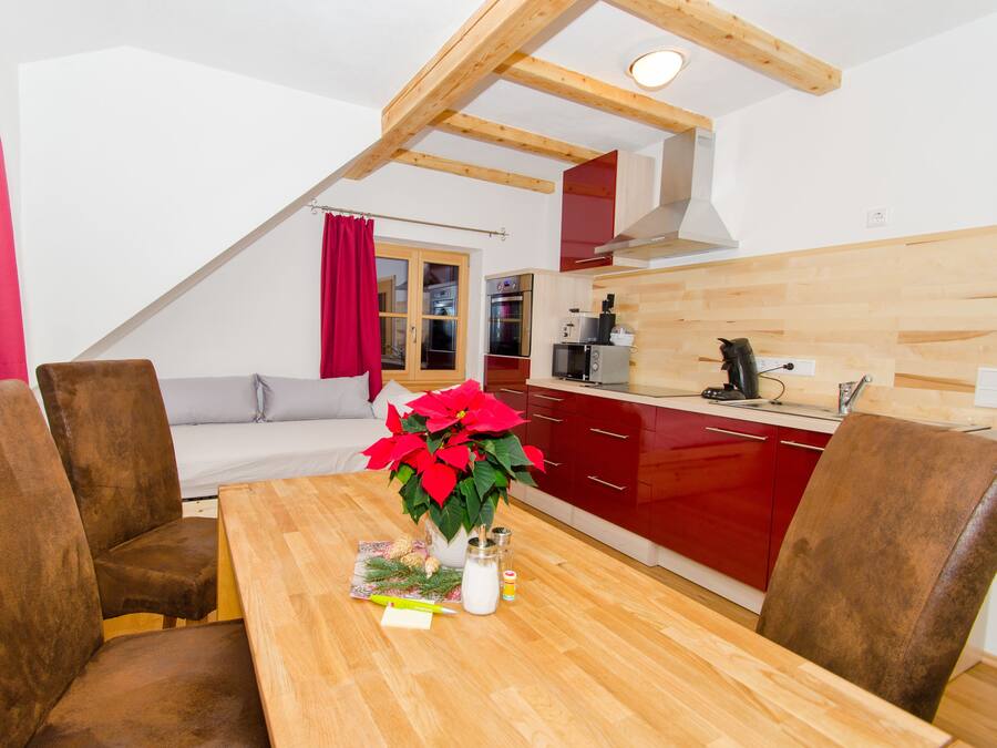 A cozy kitchen with wooden beams, a dining table with chairs, and a red kitchen counter.