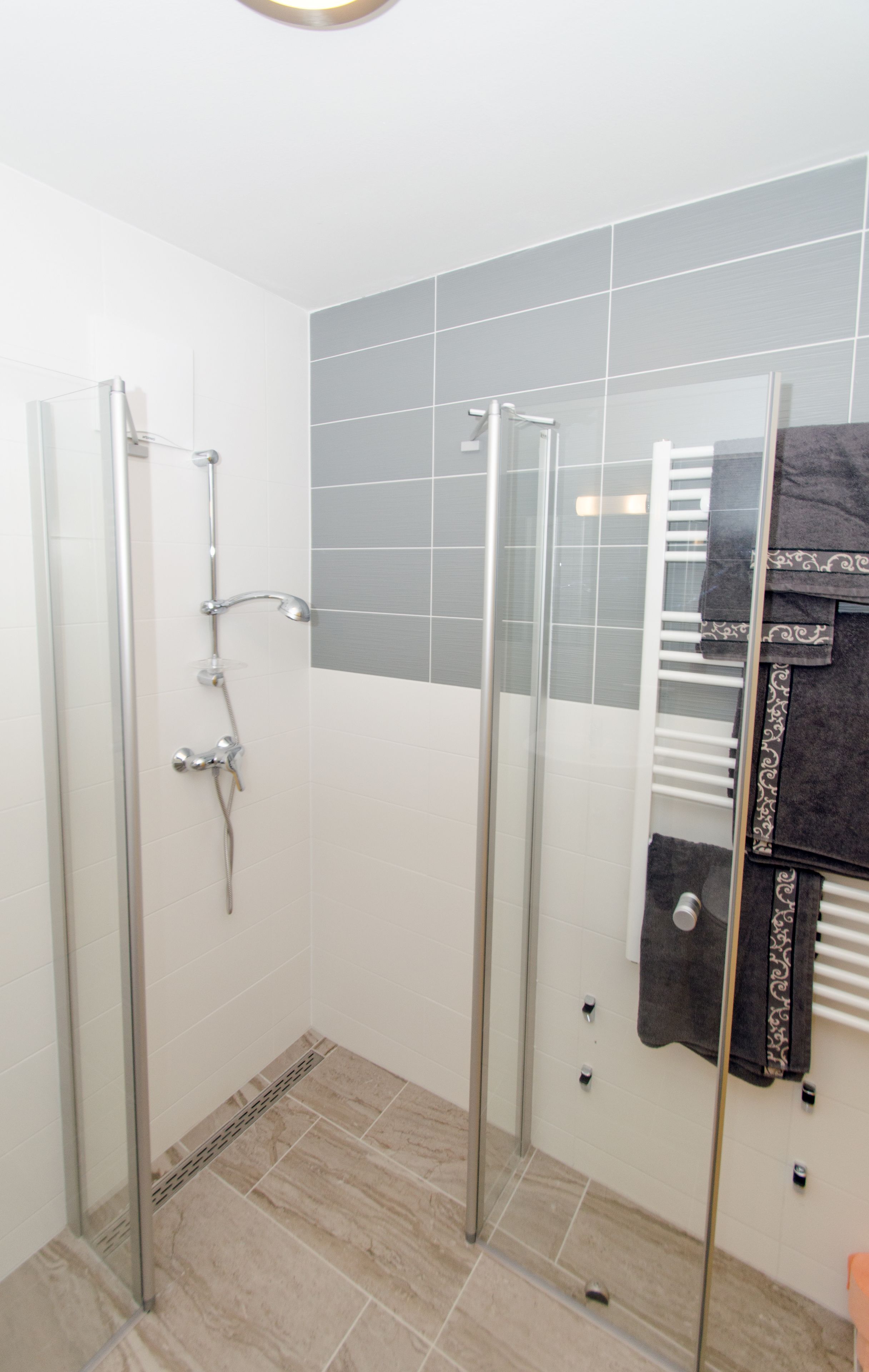 A shower area with a glass door, a towel rack, and a tiled wall.