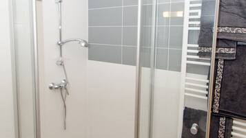 Área de chuveiro com porta de vidro, porta-toalhas e parede revestida com azulejos.
