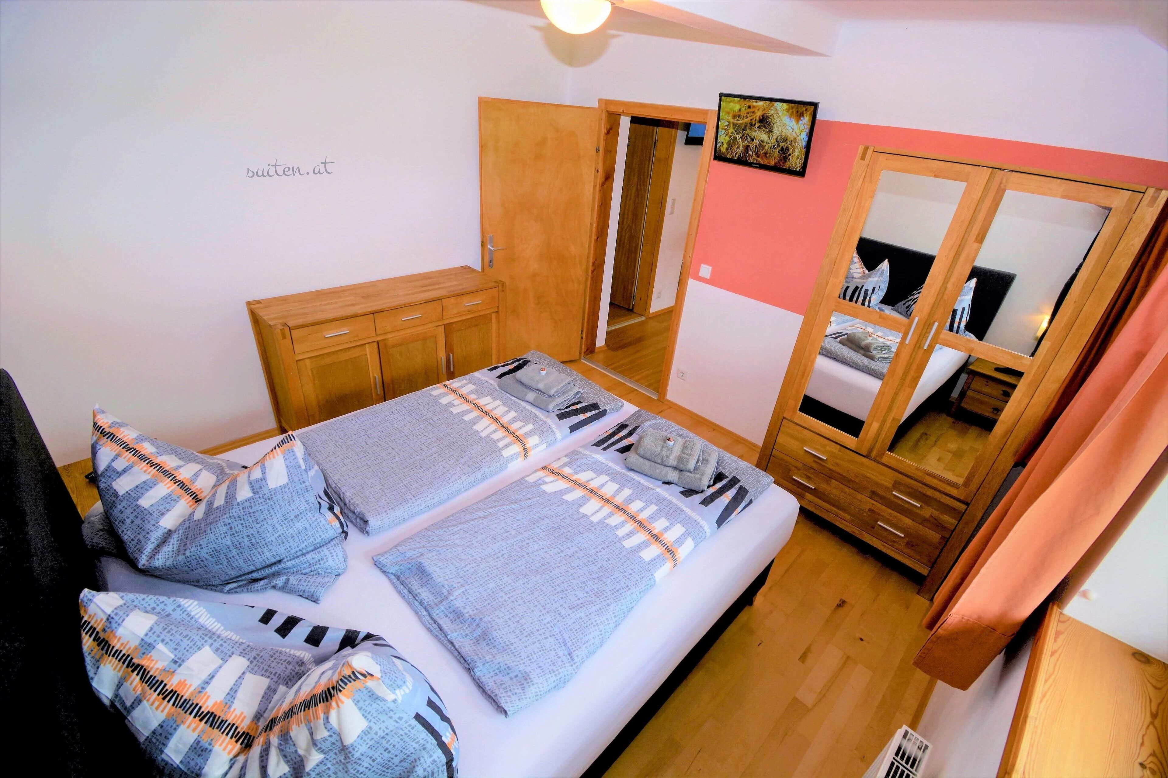 A bedroom with a bed, wooden wardrobe, and a mirror cabinet.